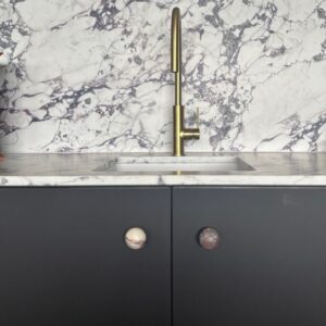 Marble kitchen sink with gold tap and black cabinets