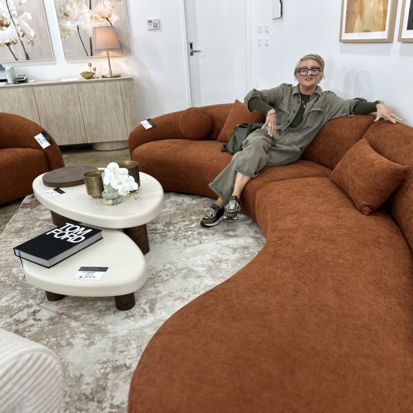 Person seated on a curved orange sofa in an interior design gallery.