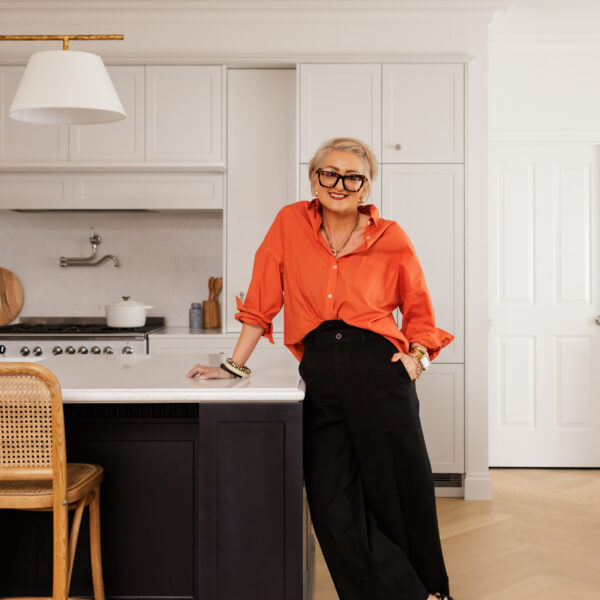 Person in modern kitchen with black island, cane chair, and orange shirt